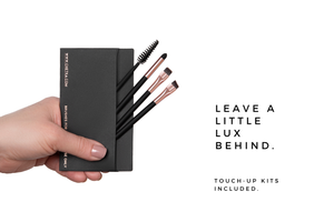 Hand holding a black makeup touch-up kit with brushes, text 'Leave a little Lux behind' on a white background.
