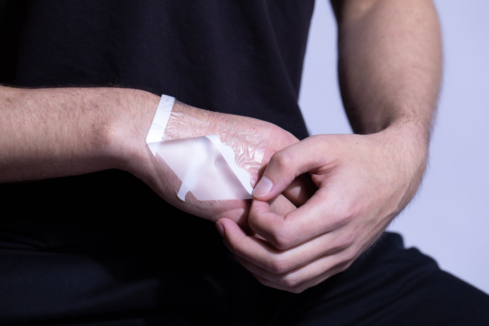 A person applying a transparent textured makeup product to the back of their hand, resembling a second skin makeup hand palette.